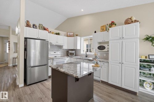 Kitchen with light stone counters, white appliances, vaulted ceiling, light wood-style floors, and white cabinets - 30 4 Heritage Way, St. Albert, AB - Indoor Photo Showing Kitchen