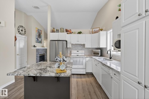 Kitchen with vaulted ceiling, light stone counters, white appliances, a center island, and white cabinetry - 30 4 Heritage Way, St. Albert, AB - Indoor Photo Showing Kitchen With Double Sink With Upgraded Kitchen
