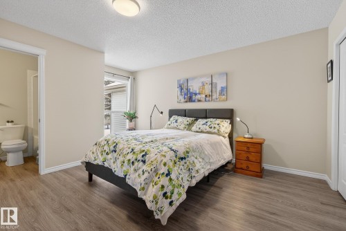 Bedroom with wood finished floors, a textured ceiling, and ensuite bath - 30 4 Heritage Way, St. Albert, AB - Indoor Photo Showing Bedroom