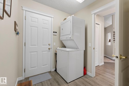 Laundry room featuring a textured ceiling, stacked washer and clothes dryer, and light wood-style flooring - 30 4 Heritage Way, St. Albert, AB - Indoor Photo Showing Laundry Room