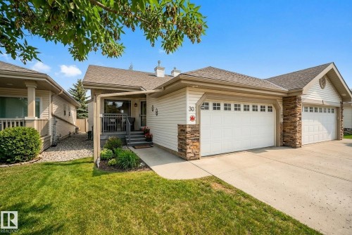 View of front of house with an attached garage, a shingled roof, driveway, covered porch, and a chimney - 30 4 Heritage Way, St. Albert, AB - Outdoor With Deck Patio Veranda With Facade