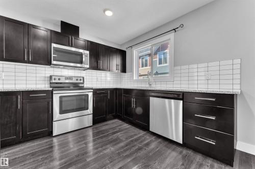 Kitchen with stainless steel appliances, light stone countertops, tasteful backsplash, dark wood-style flooring, and dark wood finish cabinetry - #38 1508 105 St Nw, Edmonton, AB - Indoor Photo Showing Kitchen With Stainless Steel Kitchen With Upgraded Kitchen