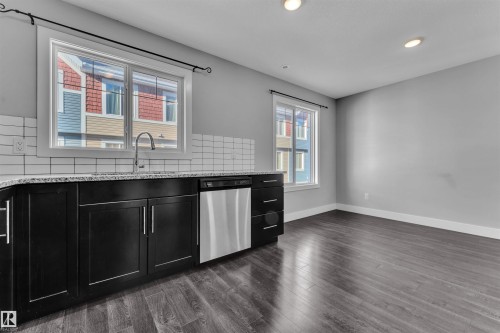 Kitchen with dark cabinetry, light stone counters, dishwasher, backsplash, and dark wood finished floors - #38 1508 105 St Nw, Edmonton, AB - Indoor Photo Showing Kitchen