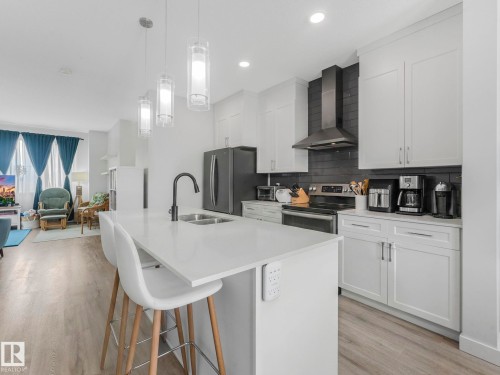 Kitchen with stainless steel appliances, an island with sink, chimney hood fan, a kitchen breakfast bar, light wood finished floors, and open floor plan - 1404 Podersky Link, Edmonton, AB - Indoor Photo Showing Kitchen With Double Sink With Upgraded Kitchen