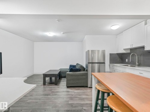 Kitchen with freestanding refrigerator, white cabinetry, light wood-style flooring, a breakfast bar, and decorative backsplash - 1404 Podersky Link, Edmonton, AB - Indoor Photo Showing Kitchen
