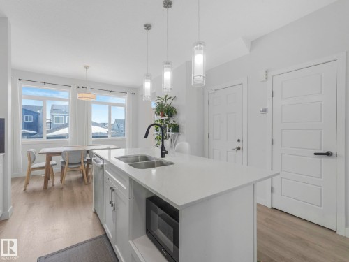 Kitchen with light wood-type flooring, decorative light fixtures, black microwave, a kitchen island with sink, and light stone counters - 1404 Podersky Link, Edmonton, AB - Indoor Photo Showing Kitchen With Double Sink With Upgraded Kitchen