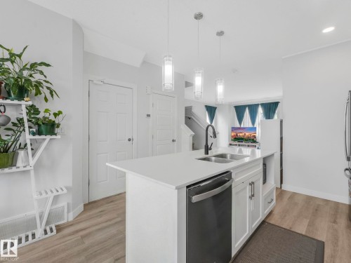 Kitchen featuring stainless steel dishwasher, white cabinetry, hanging light fixtures, a kitchen island with sink, and light wood-style flooring - 1404 Podersky Link, Edmonton, AB - Indoor Photo Showing Kitchen With Double Sink