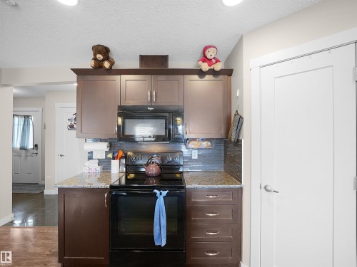 Kitchen featuring black appliances, dark wood finish cabinetry, light stone counters, tasteful backsplash, and a textured ceiling - 1659 Hammond Crescent, Edmonton, AB - Indoor Photo Showing Kitchen
