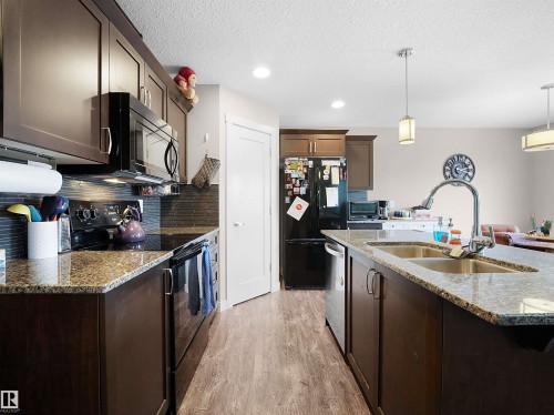 Kitchen featuring black appliances, dark stone countertops, dark wood finish cabinets, decorative light fixtures, and light wood finished floors - 1659 Hammond Crescent, Edmonton, AB - Indoor Photo Showing Kitchen With Double Sink With Upgraded Kitchen