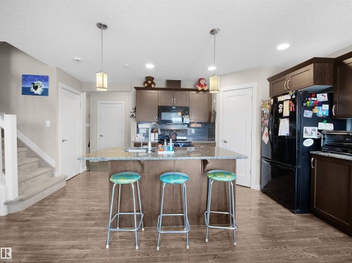 Kitchen featuring dark wood finish cabinetry, a kitchen bar, light stone countertops, black appliances, and a textured ceiling - 1659 Hammond Crescent, Edmonton, AB - Indoor Photo Showing Kitchen With Upgraded Kitchen