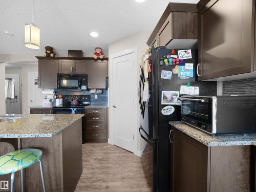 Kitchen featuring dark wood finish cabinets, tasteful backsplash, black appliances, light stone counters, and a textured ceiling - 1659 Hammond Crescent, Edmonton, AB - Indoor Photo Showing Kitchen