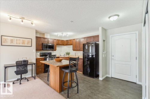 Kitchen featuring black appliances, a kitchen island, a breakfast bar area, light countertops, and a textured ceiling - 112 5340 199 Street, Edmonton, AB - Indoor Photo Showing Kitchen