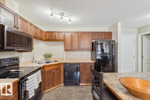Kitchen with black appliances, light countertops, a textured ceiling, and wood finish cabinets - 112 5340 199 Street, Edmonton, AB - Indoor Photo Showing Kitchen With Double Sink