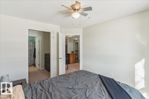 Bedroom featuring light carpet, a textured ceiling, ceiling fan, and ensuite bath - 112 5340 199 Street, Edmonton, AB - Indoor Photo Showing Bedroom