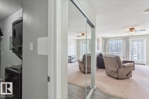 Living room featuring a textured ceiling, ceiling fan, stacked washer and dryer, and carpet flooring - 112 5340 199 Street, Edmonton, AB - Indoor Photo Showing Other Room