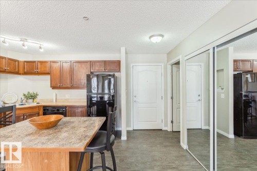 Kitchen with light countertops, black appliances, wood finish cabinetry, a kitchen bar, and a textured ceiling - 112 5340 199 Street, Edmonton, AB - Indoor Photo Showing Kitchen