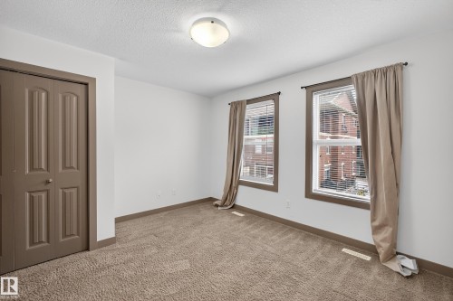 The property features a bright room with two windows, complete with blinds and curtains, offering views of the surrounding buildings - 1649 Cunningham Way, Edmonton, AB - Indoor Photo Showing Other Room