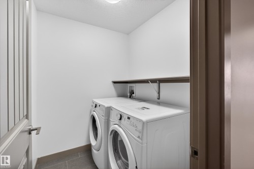 Dedicated laundry area featuring a washer and dryer, tile flooring, and a wall-mounted shelf - 1649 Cunningham Way, Edmonton, AB - Indoor Photo Showing Laundry Room
