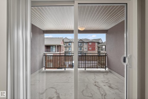 The property features a balcony with a concrete floor, dark railing, and a slatted ceiling, offering views of buildings - 1649 Cunningham Way, Edmonton, AB - Indoor Photo Showing Other Room