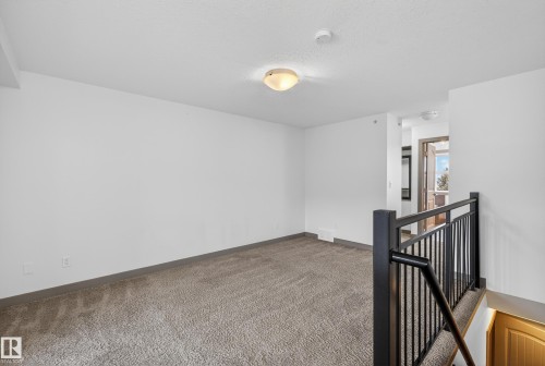 This room features wall-to-wall carpeting, a flush mount ceiling light fixture, and a dark-colored metal stair railing - 1649 Cunningham Way, Edmonton, AB - Indoor Photo Showing Other Room