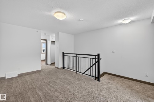 Open concept space featuring neutral-toned carpeting, white walls, and a black metal railing - 1649 Cunningham Way, Edmonton, AB - Indoor Photo Showing Other Room