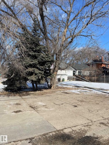 The property features mature trees, including evergreen trees, and a paved surface - 8915 99 Street Nw, Edmonton, AB 