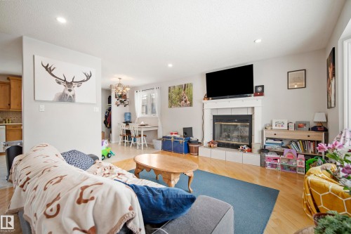 Living area featuring a tiled fireplace, light wood-type flooring, and suspended lighting - 9221 84 Street, Fort Saskatchewan, AB - Indoor Photo Showing Living Room With Fireplace