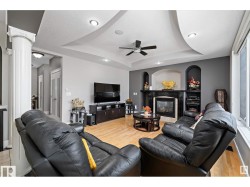 Living area featuring ceiling fan, a fireplace, ornate columns, recessed lighting, and light wood-style floors - 