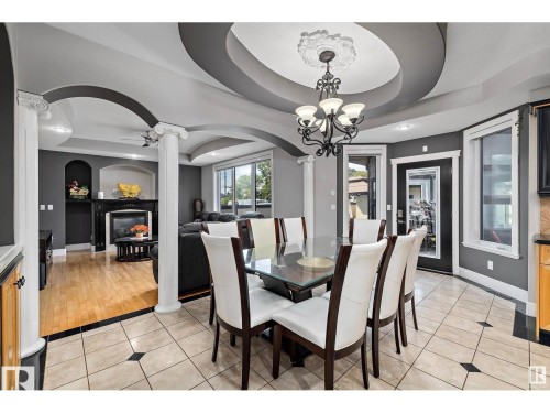 Dining area featuring a tray ceiling, ceiling fan, light tile patterned floors, a glass covered fireplace, and hanging lights - 9544 154 Street, Edmonton, AB 