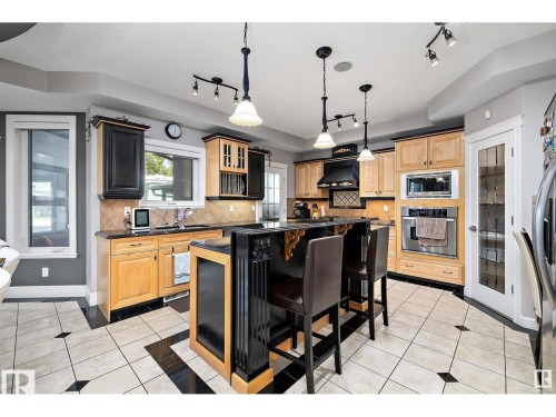 Kitchen with light tile patterned flooring, stainless steel appliances, a breakfast bar area, backsplash, and light wood finish cabinetry - 9544 154 Street, Edmonton, AB 