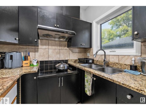 Kitchen featuring dark cabinets, light stone countertops, decorative backsplash, and black electric stovetop - 9544 154 Street, Edmonton, AB 