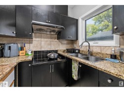 Kitchen featuring dark cabinets, light stone countertops, decorative backsplash, and black electric stovetop - 