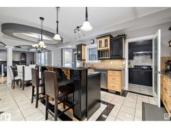 Kitchen featuring light tile patterned floors, glass fronted cabinets, dishwasher, a breakfast bar area, and a raised ceiling - 