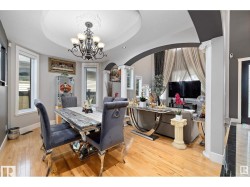 Dining space with arched walkways, decorative columns, light wood-style floors, a tray ceiling, and hanging lights - 