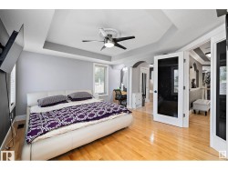 Bedroom with a raised ceiling, light wood-style flooring, arched walkways, and a ceiling fan - 