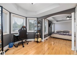 Bedroom featuring a raised ceiling, light wood-style flooring, multiple windows, arched walkways, and a ceiling fan - 
