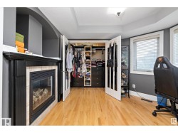 Walk in closet with light wood-style floors, a tiled fireplace, and a tray ceiling - 