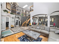 Living room with hanging lights, arched walkways, ornate columns, light wood-style floors, and a high ceiling - 
