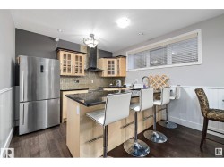 Kitchen featuring wainscoting, light wood finish cabinets, freestanding refrigerator, a kitchen bar, and a peninsula - 