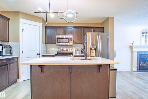 Kitchen featuring a kitchen breakfast bar, dark wood finish cabinets, and a textured ceiling - 2224 Austin Way, Edmonton, AB - Indoor Photo Showing Kitchen With Stainless Steel Kitchen With Double Sink With Upgraded Kitchen