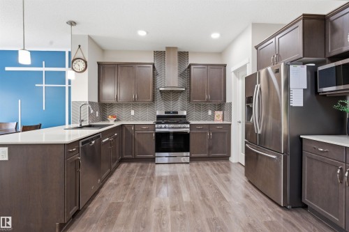 Kitchen with dark wood finish cabinets, stainless steel appliances, a peninsula, light wood-style floors, and decorative light fixtures - 5112 Andison Close, Edmonton, AB - Indoor Photo Showing Kitchen With Upgraded Kitchen
