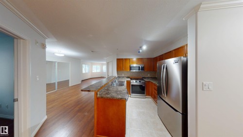 Kitchen featuring stainless steel appliances, wood finish cabinets, a peninsula, tasteful backsplash, and ornamental molding - 115 9938 104 St, Edmonton, AB - Indoor Photo Showing Kitchen