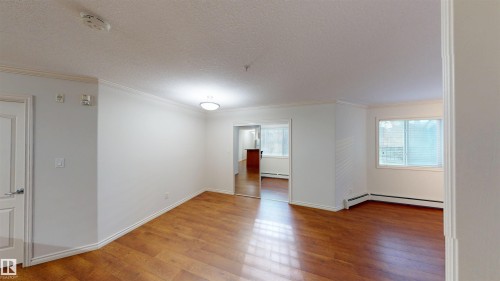 Unfurnished room featuring hardwood / wood-style floors, crown molding, a textured ceiling, a smoke detector, and baseboard heating - 115 9938 104 St, Edmonton, AB - Indoor Photo Showing Other Room