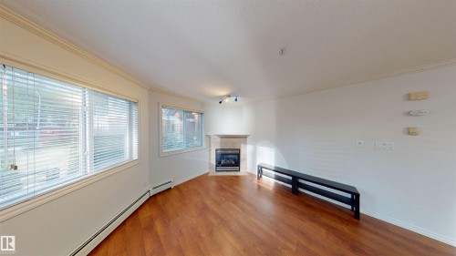 Unfurnished living room featuring a baseboard heating unit, wood finished floors, ornamental molding, and a tile fireplace - 115 9938 104 St, Edmonton, AB - Indoor With Fireplace