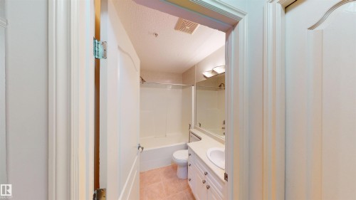 Full bath with vanity, a textured ceiling, bathing tub / shower combination, and light tile patterned floors - 115 9938 104 St, Edmonton, AB - Indoor Photo Showing Bathroom