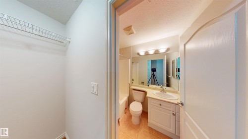 Bathroom with a textured ceiling, vanity, shower / bath combo, and light tile patterned floors - 115 9938 104 St, Edmonton, AB - Indoor Photo Showing Bathroom