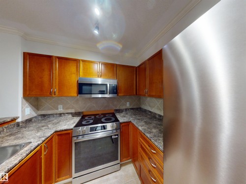 Kitchen with stainless steel appliances, wood finish cabinets, ornamental molding, backsplash, and light tile patterned floors - 115 9938 104 St, Edmonton, AB - Indoor Photo Showing Kitchen