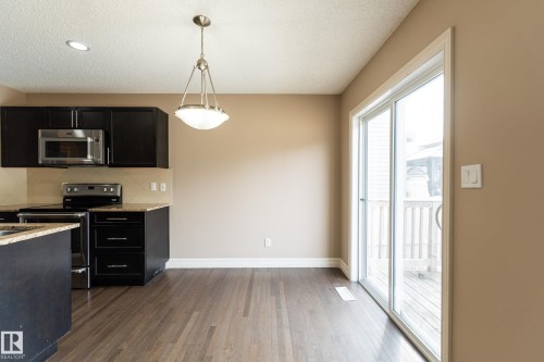 Kitchen with dark cabinets, stainless steel appliances, light stone counters, dark wood finished floors, and hanging light fixtures - 1118 162 Street, Edmonton, AB - Indoor Photo Showing Kitchen