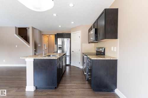 Kitchen with stainless steel appliances, light stone countertops, a center island with sink, dark wood-style floors, and a textured ceiling - 1118 162 Street, Edmonton, AB - Indoor Photo Showing Kitchen With Upgraded Kitchen