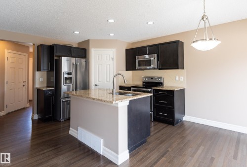 Kitchen with light stone counters, stainless steel appliances, tasteful backsplash, dark wood-style floors, and a center island with sink - 1118 162 Street, Edmonton, AB - Indoor Photo Showing Kitchen With Stainless Steel Kitchen With Upgraded Kitchen